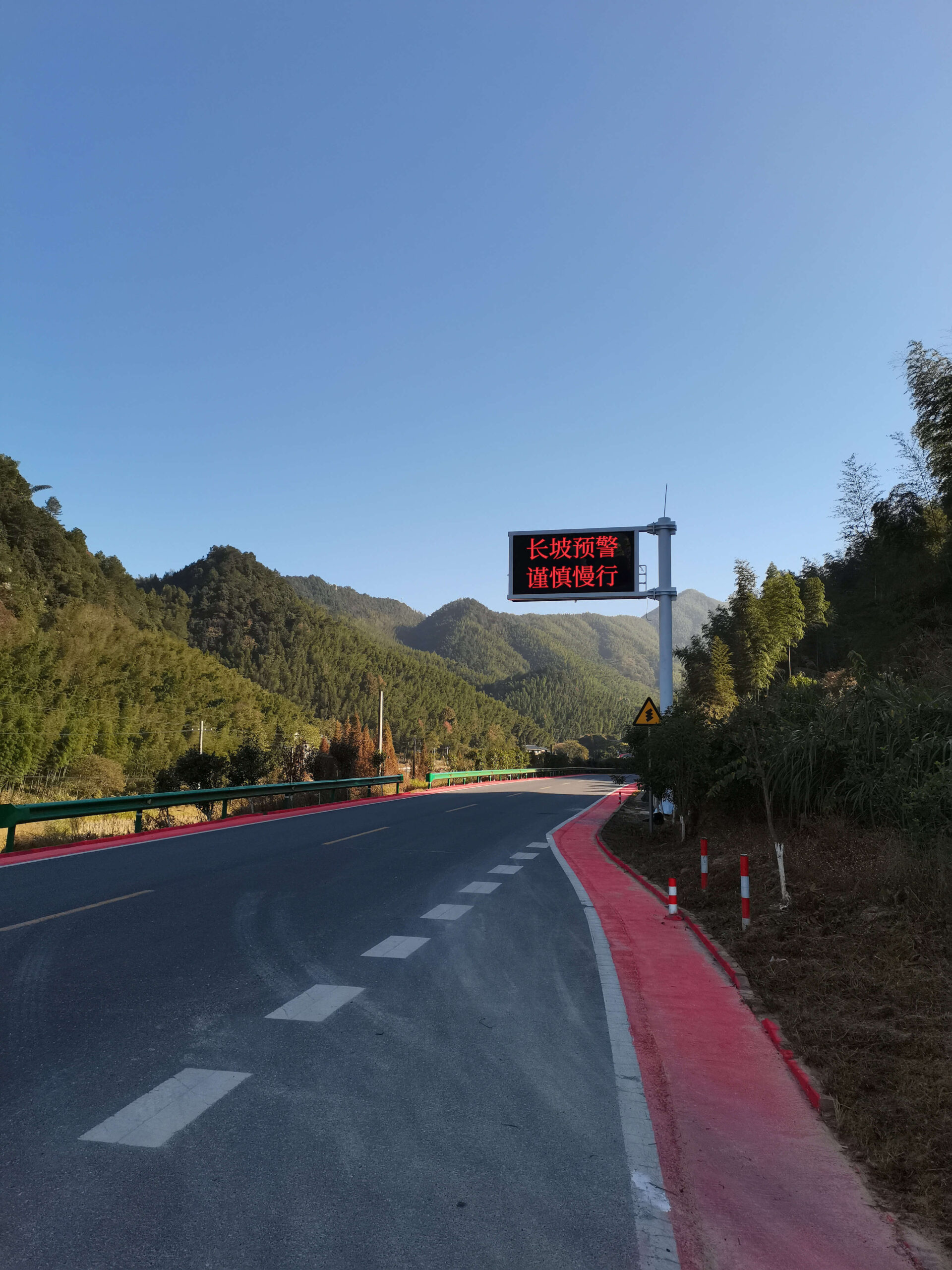 Intelligent Variable Message Sign (VMS) installed on a highway gantry, displaying a caution message for ongoing road construction and encouraging slow driving